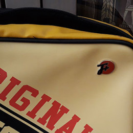 a cream yellow and red bag that says ORIGINAL and has an F Plus pin