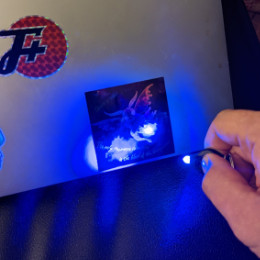 a moffman sticker on a laptop displays a message under blacklight